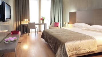 Une chambre d’hôtel comprenant un lit, un bureau avec un téléviseur à écran plat, une chaise, une petite table avec un vase de fleurs et une table de chevet avec une lampe.