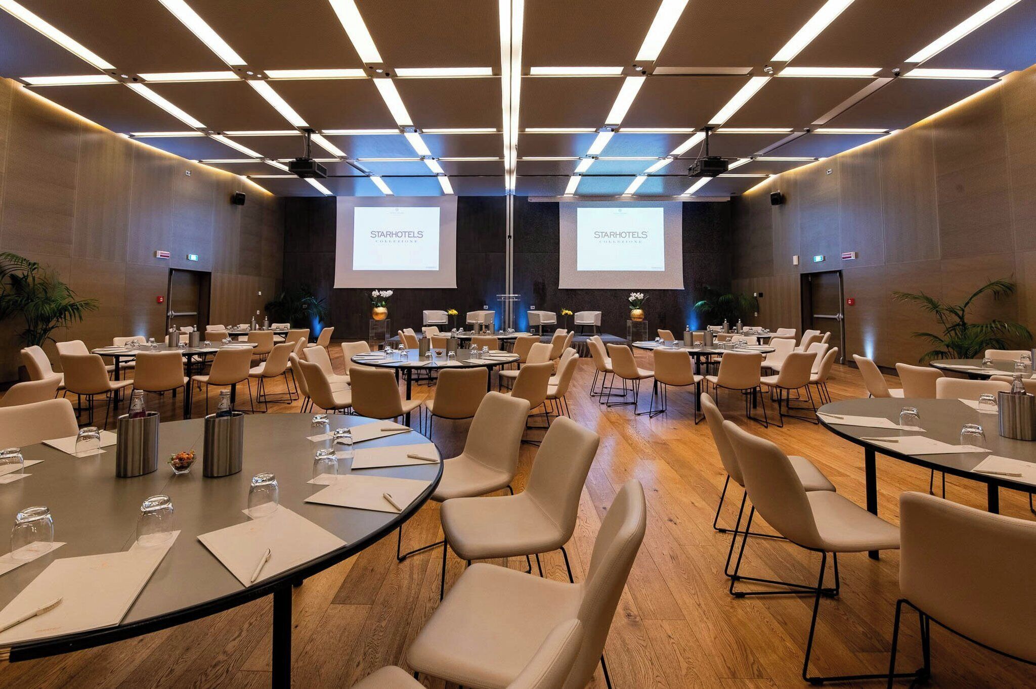 A conference room with multiple tables and chairs, equipped with projectors and screens displaying 'StarHotels Collection'.