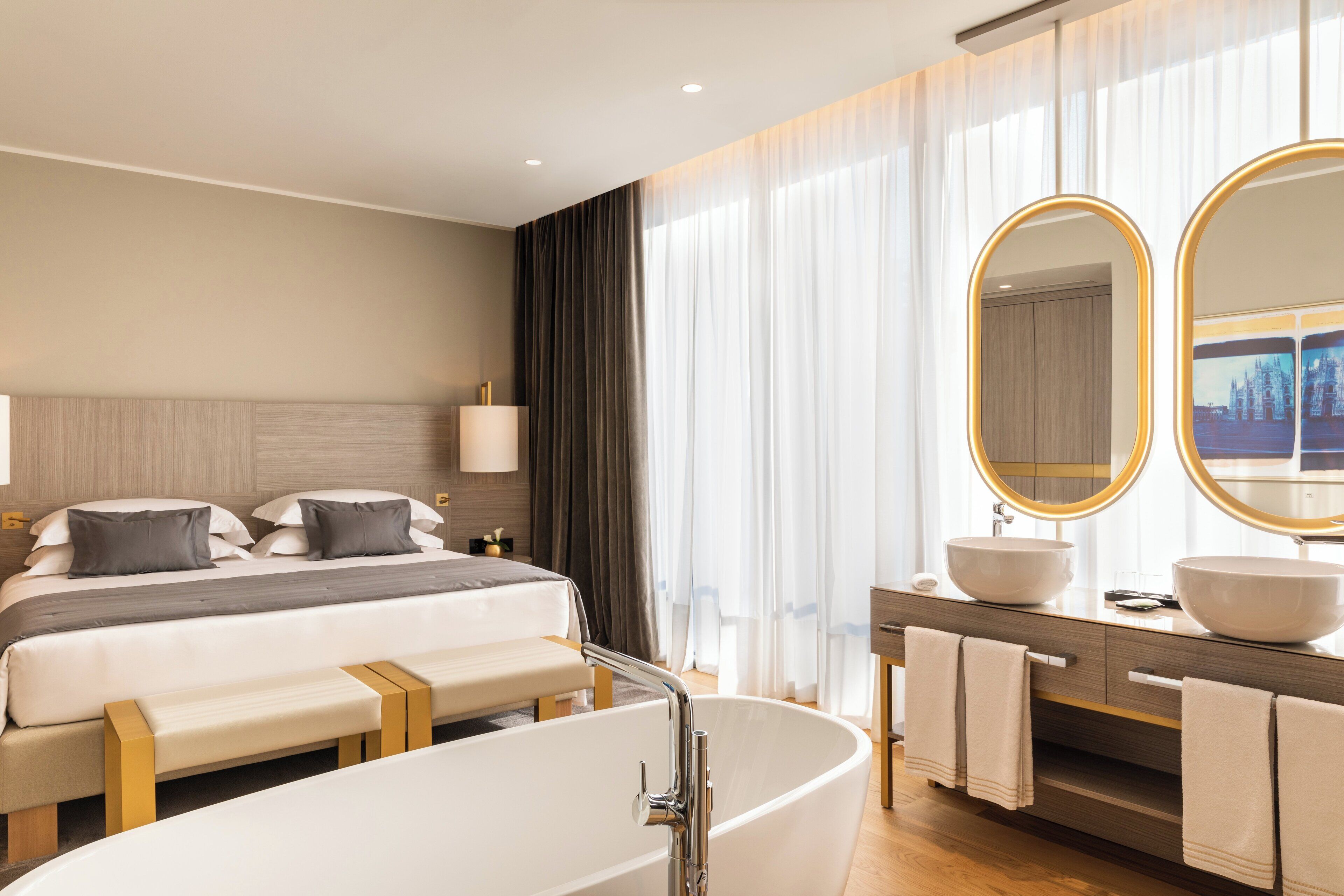 Una habitación de hotel moderna con una cama grande, una bañera, un tocador con dos lavamanos y un espejo amplio.