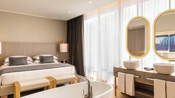 Una habitación de hotel moderna con una cama grande, una bañera, un tocador con dos lavamanos y un espejo amplio.