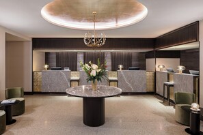A modern reception area with a marble reception desk, a central round table with a vase of flowers, and a unique chandelier.