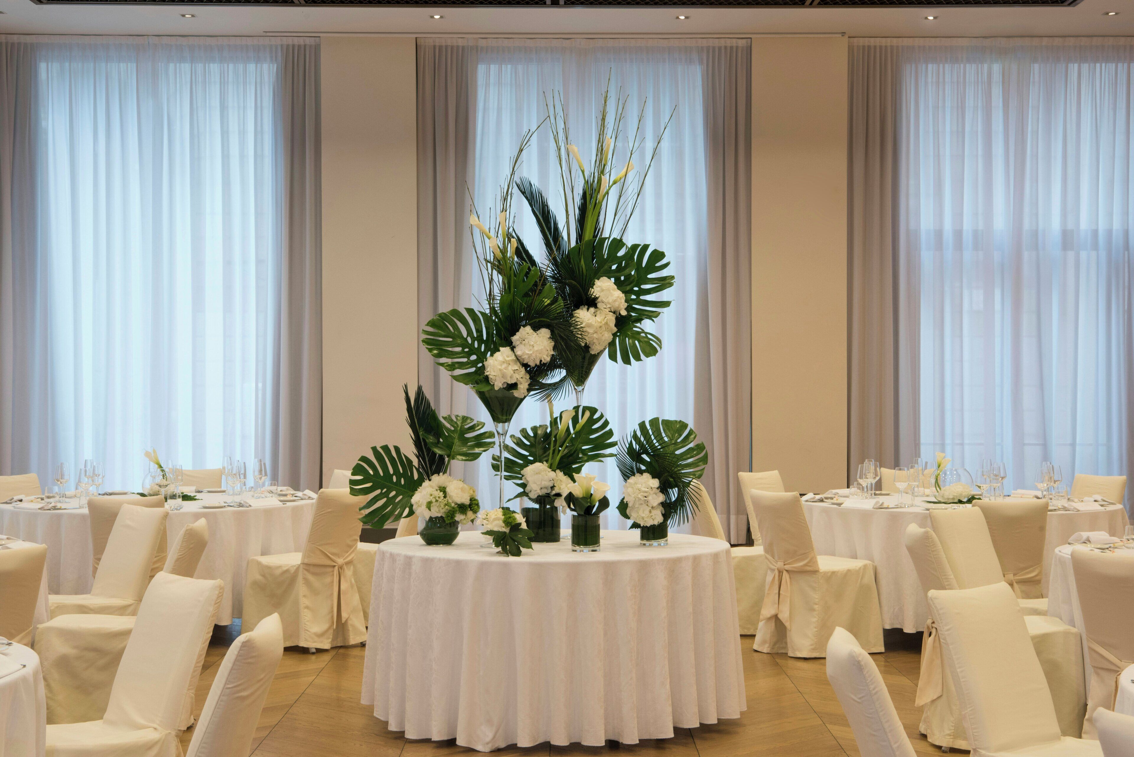 Un salón de banquetes con mesas redondas, manteles blancos y sillas.