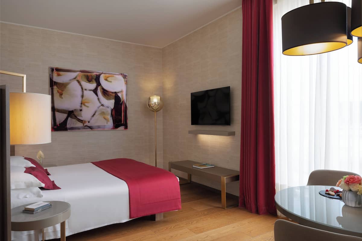 Une chambre d’hôtel comprenant un lit, une table de chevet, une lampe, une télévision et un coin repas avec une table et des chaises.
