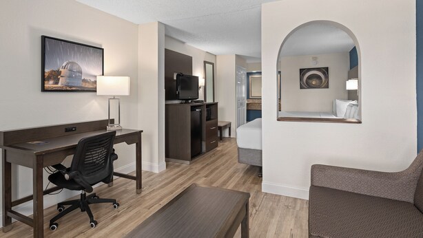 A hotel room with a desk, office chair, and a bed. There is a television and a small table. - Baymont by Wyndham Orlando East (Orlando)