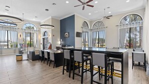 A modern hotel lobby with a long bar, multiple seating areas, and large windows offering views. - Baymont by Wyndham Orlando East (Orlando)