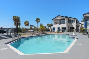 A swimming pool with a clear blue water, surrounded by a fence, and a building with a modern design in the background. - Baymont by Wyndham Orlando East (Orlando)