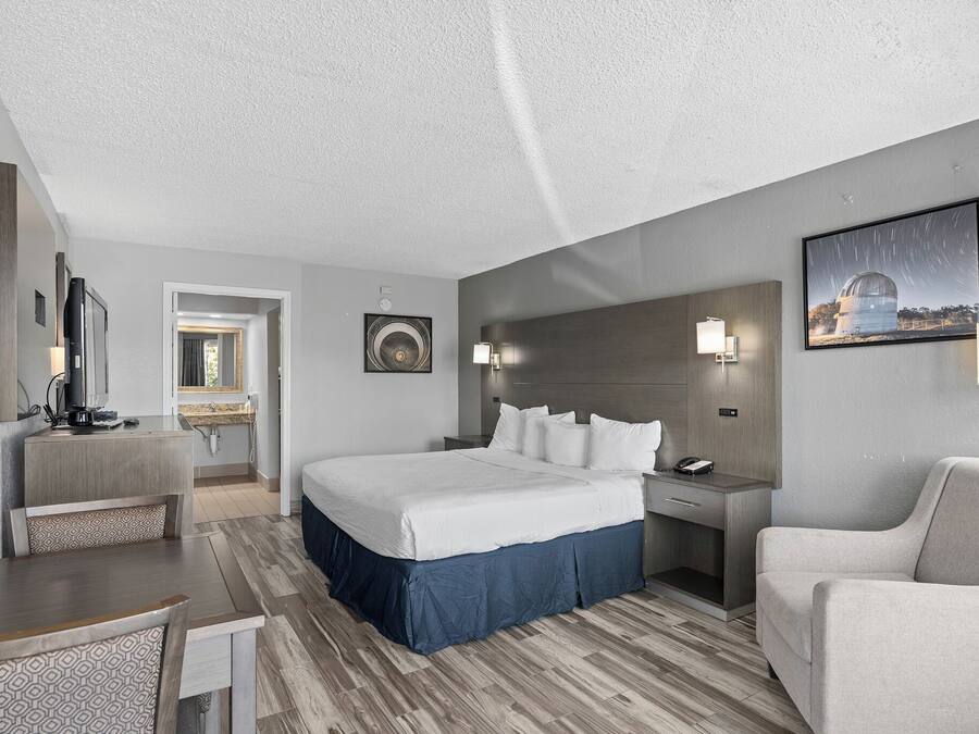 Een hotelkamer met een bed, een bureau, een stoel, een nachtkastje en een aan de muur bevestigde televisie.