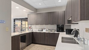 A modern kitchen with dark wood cabinets, a white countertop, a built-in dishwasher, a coffee machine, and a sink. - Baymont by Wyndham Orlando East (Orlando)