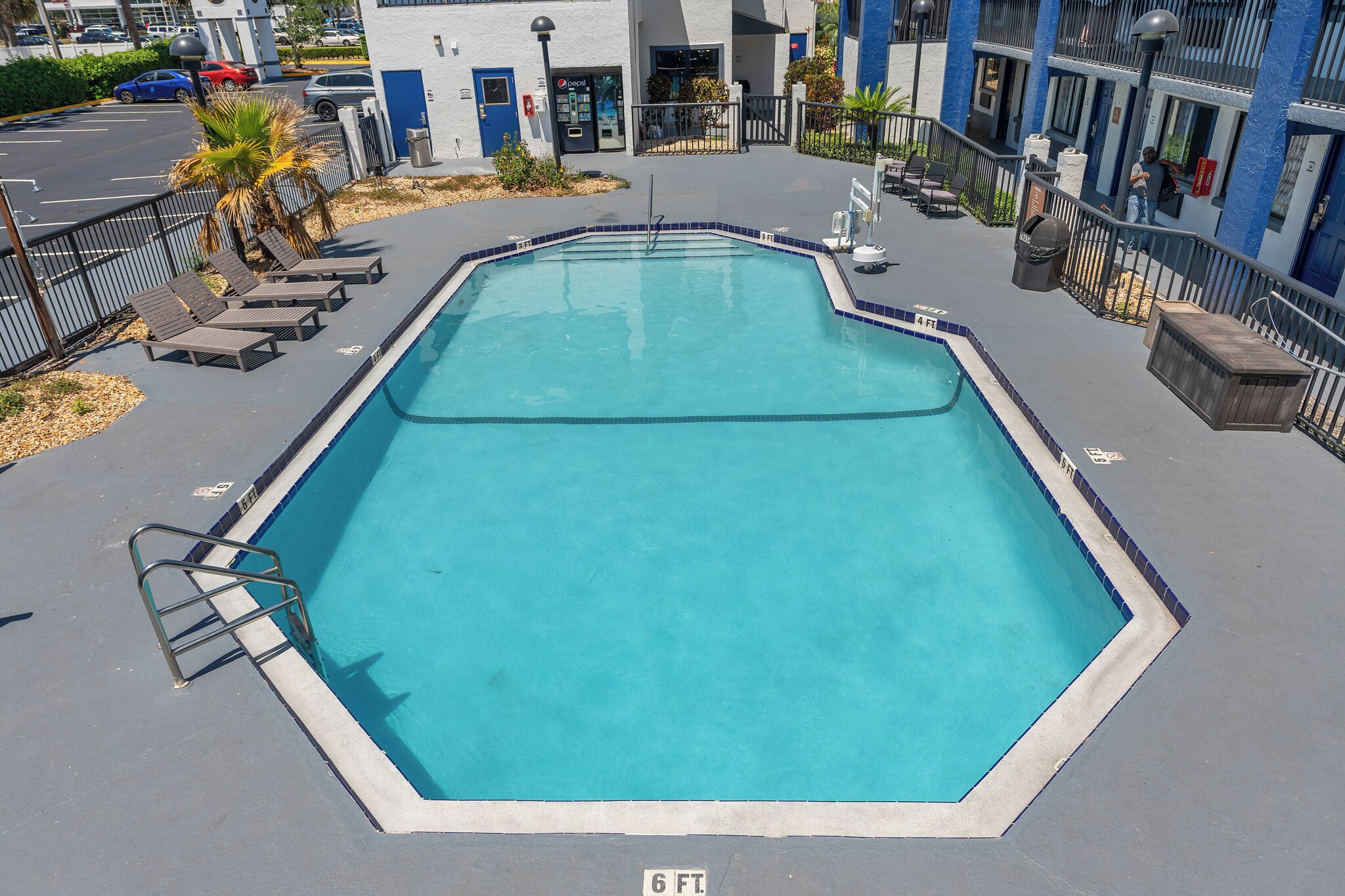 Piscina retangular com marcação de profundidade de 1,8 metros, rodeada por espreguiçadeiras e uma escada de metal.