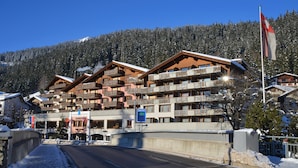 A ski resort with multiple chalet-style buildings, a clear sky, and a snowy mountain backdrop. - Silvretta Parkhotel (Klosters-Serneus)