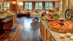 A restaurant with wooden interiors, multiple tables, and a buffet with various food items. - Silvretta Parkhotel (Klosters-Serneus)