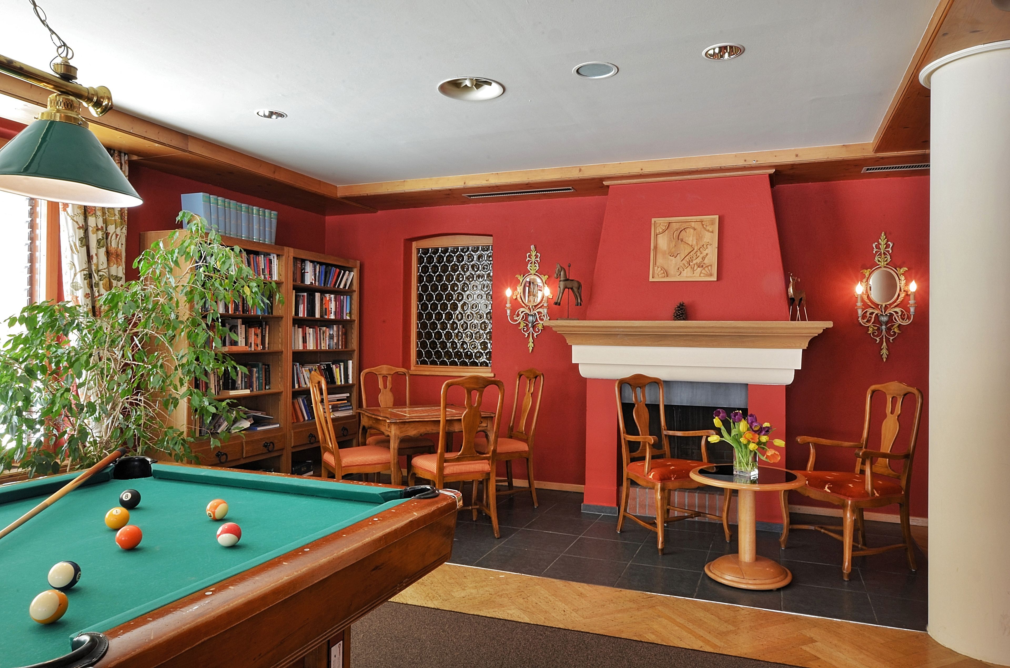 A billiards room with a pool table, chairs, a fireplace, and a bookshelf.