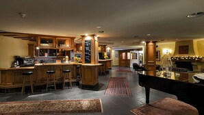 A spacious kitchen with a bar area, wooden cabinets, and a piano. - Silvretta Parkhotel (Klosters-Serneus)