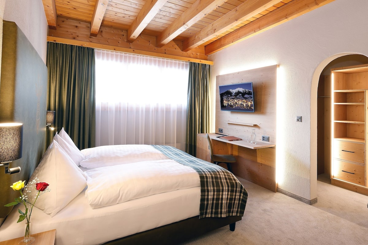 Hotellihuone, jossa on sänky, työpöytä, televisio ja puinen vaatekaappi.