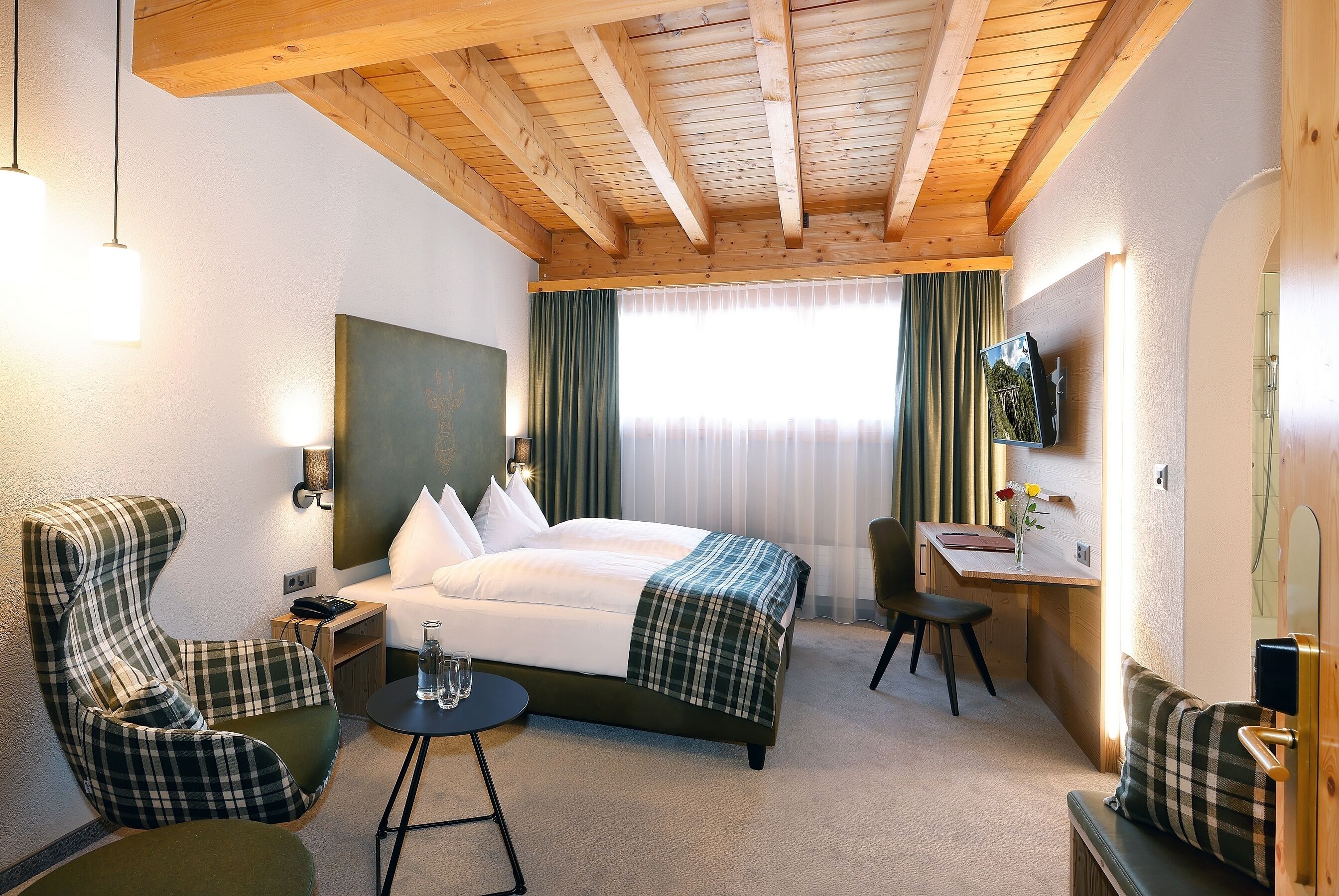 A hotel room with a bed, two chairs, a desk, and a TV.