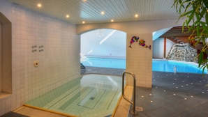 A modern indoor swimming pool area with a glass wall, a stone wall, and a colorful mural. - Silvretta Parkhotel (Klosters-Serneus)
