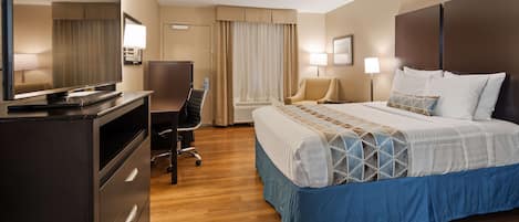 A hotel room with a bed, desk, chair, television, and a large mirror.