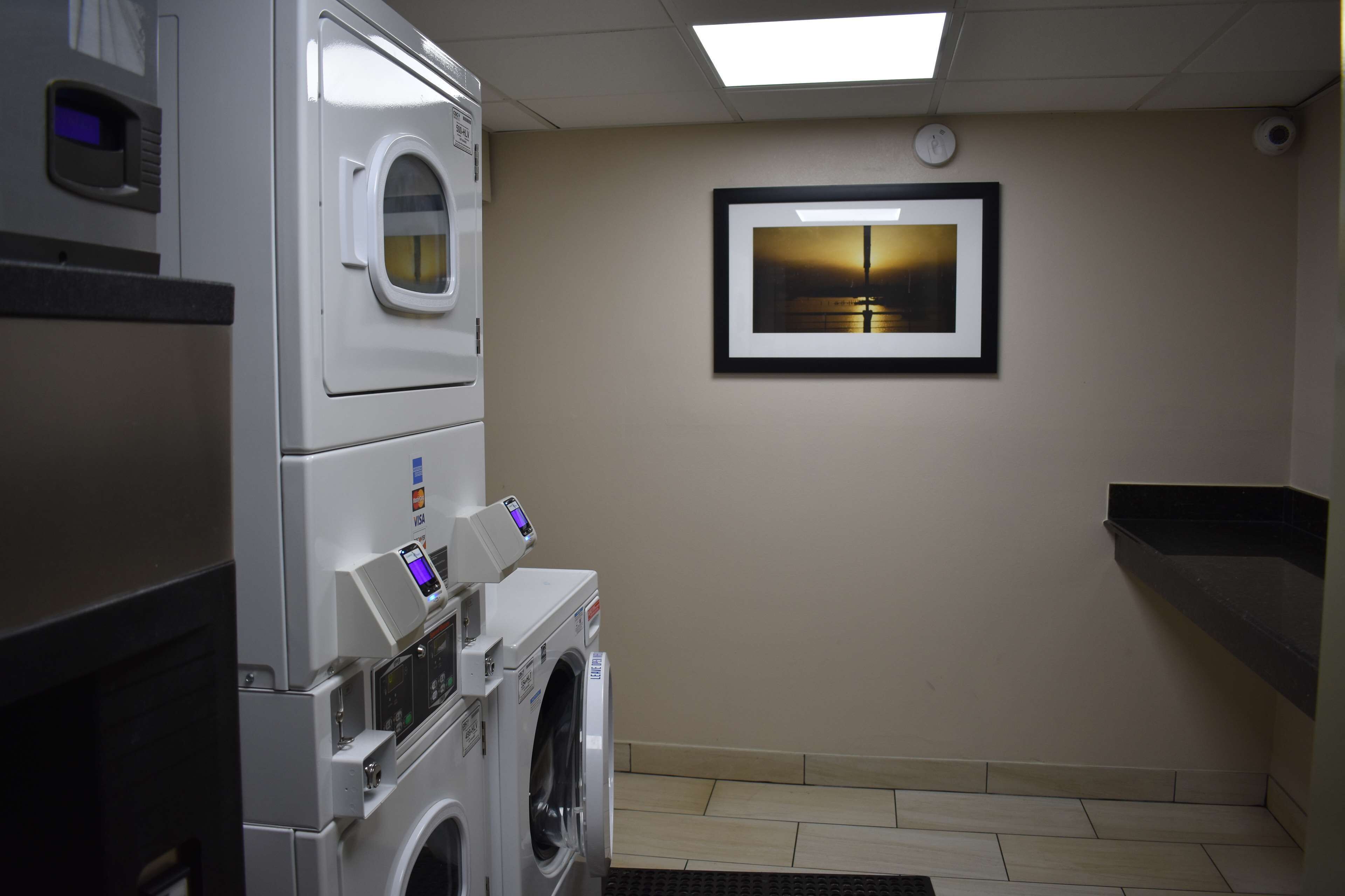 A laundry room with stacked washers and dryers, a framed picture on the wall, and a black countertop.