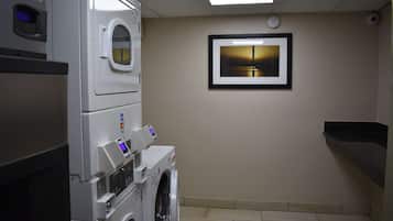 A laundry room with stacked washers and dryers, a framed picture on the wall, and a black countertop.