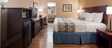 A hotel room with a bed, desk, refrigerator, and a mirror.