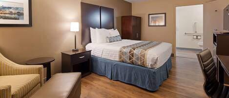 Habitación de hotel con cama, escritorio, silla, una mesita y baño visible a través de una puerta abierta.