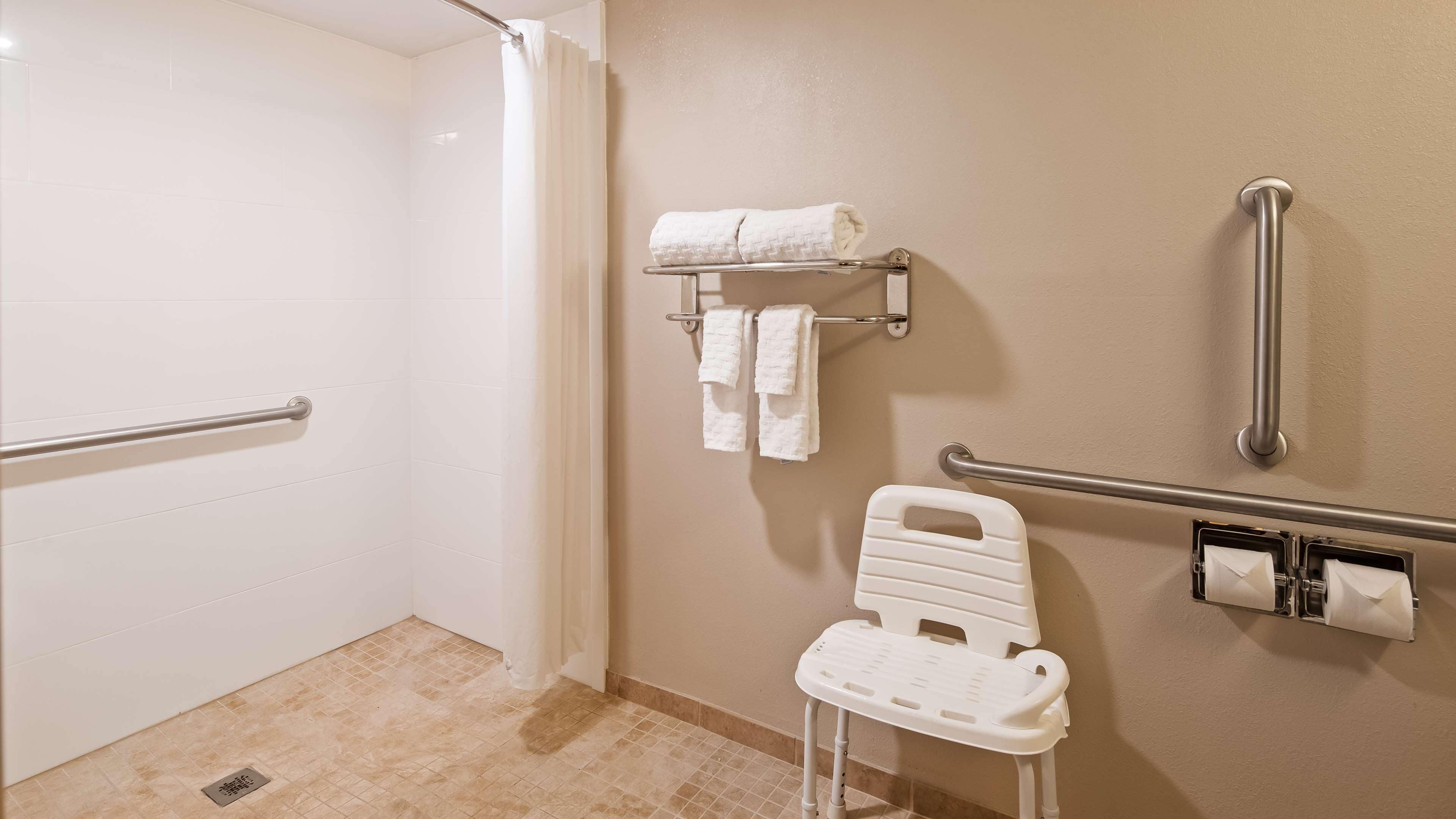 A bathroom with a shower, grab bars, a wheelchair-accessible bench, and towel racks.