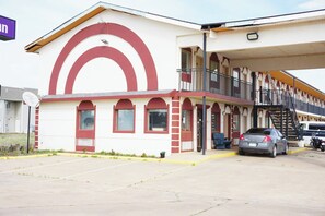 A building with a red and white facade, a balcony, and a parking area with cars.