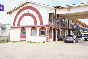 Un edificio con fachada roja y blanca, un balcón y un estacionamiento con coches.