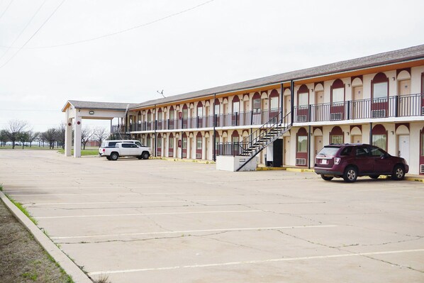 A motel with a parking lot, a covered walkway, and a staircase leading to the entrance.
