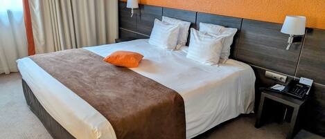 Hotellihuone, jossa on suuri sänky, kaksi yöpöytävalaisinta, puhelin ja matolla peitetty lattia.