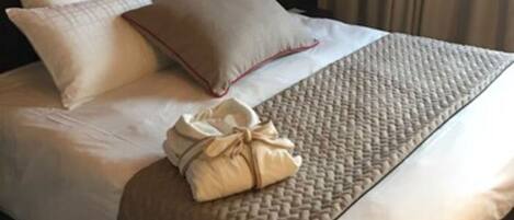 A neatly made bed with a beige blanket and pillows, a brown woven throw blanket, and a towel on the side.