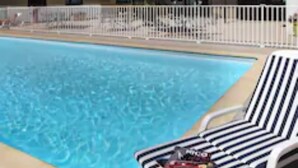 A swimming pool with lounge chairs, a hotel building with multiple floors and windows, and a white fence surrounding the pool area. - Alexander Park Chambéry (Chambery)