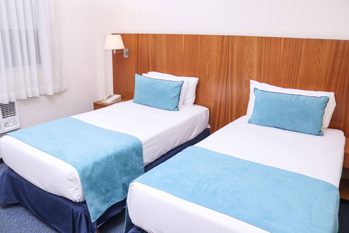 Two single beds with blue and white bedding, a wooden headboard, a bedside lamp, and a phone on the nightstand.
