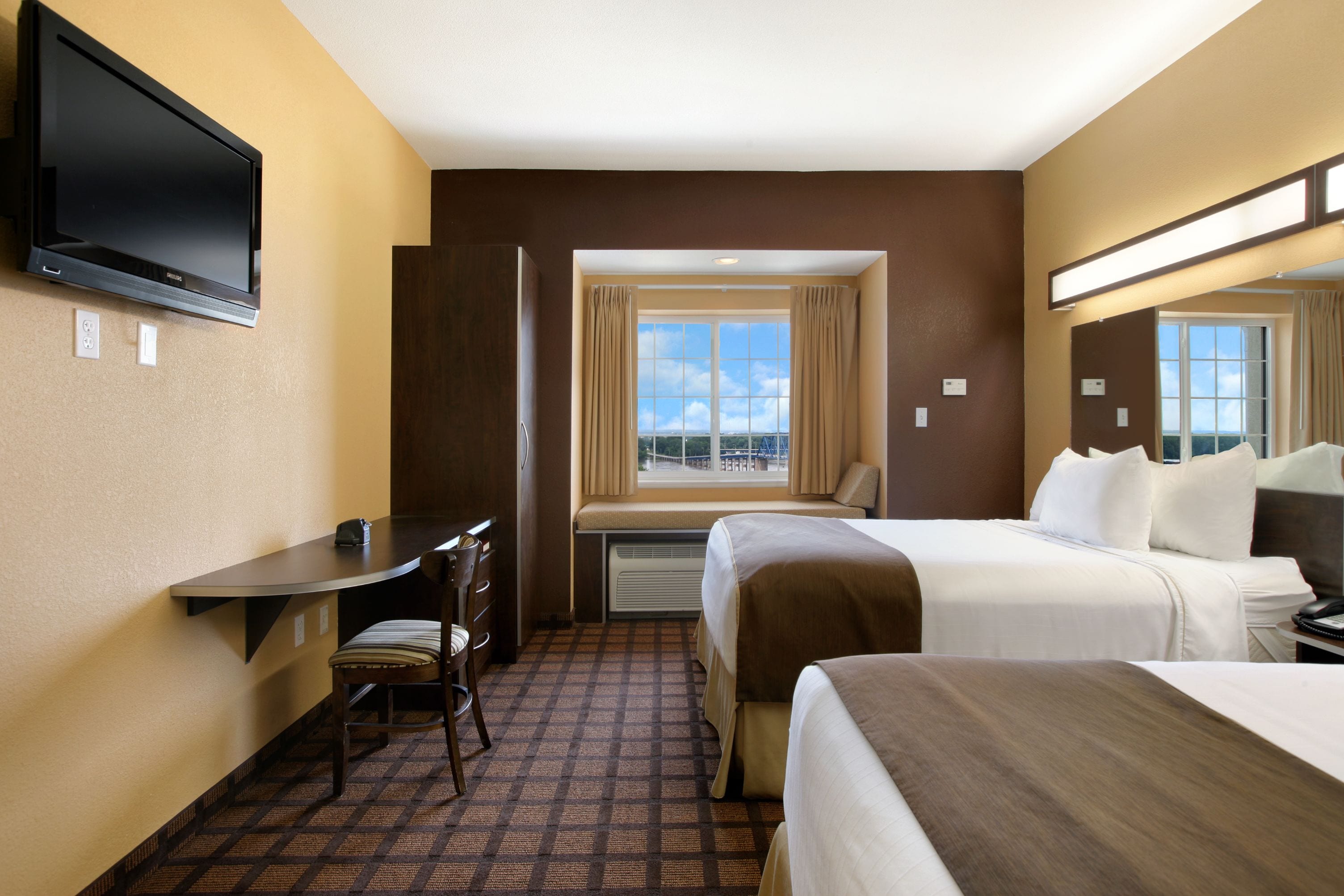 A hotel room with two beds, a desk, a chair, a TV, and a window with a view.