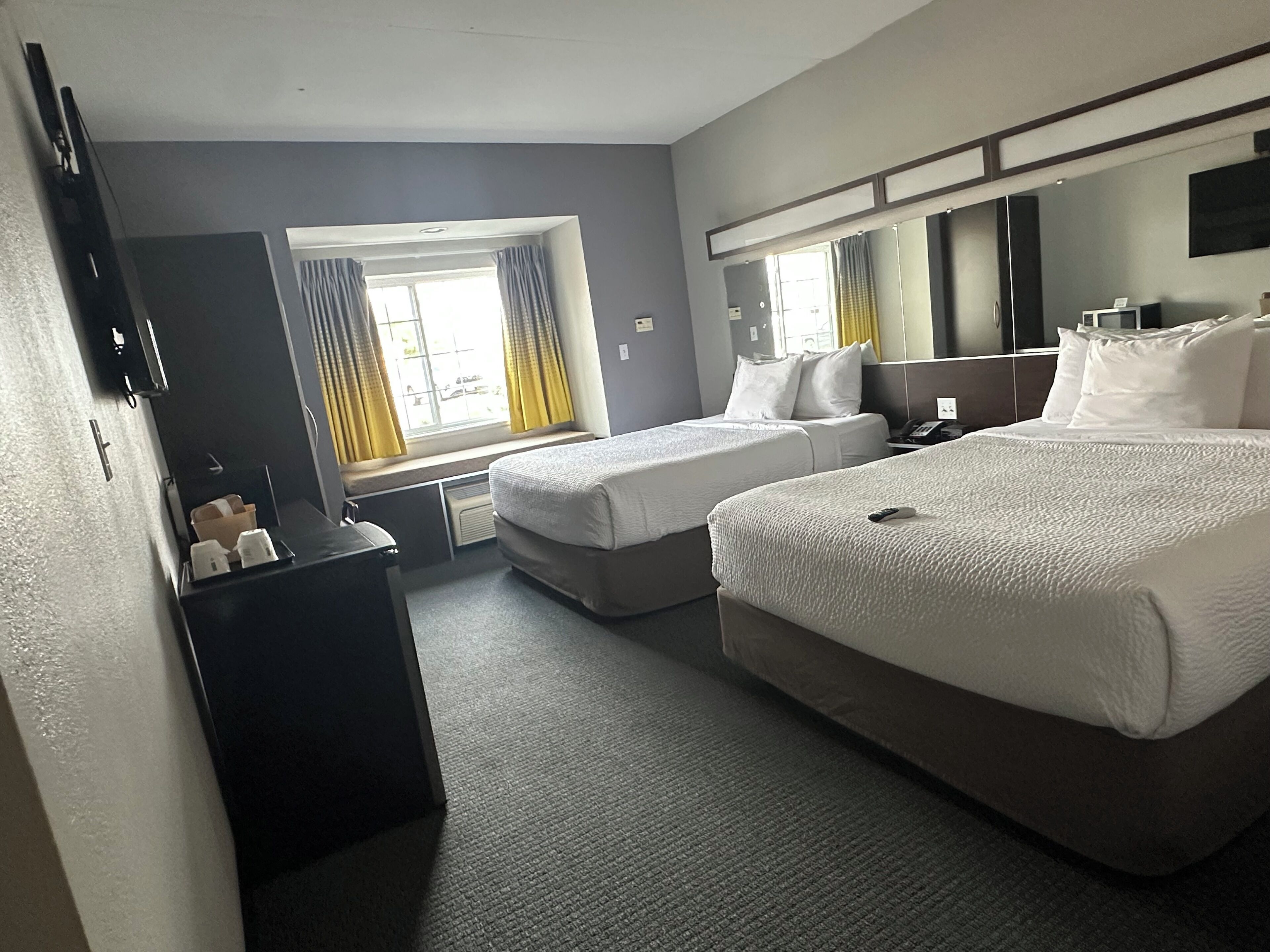 A hotel room with two single beds, a large bed, a desk with a chair, a mirror, and a window with curtains.