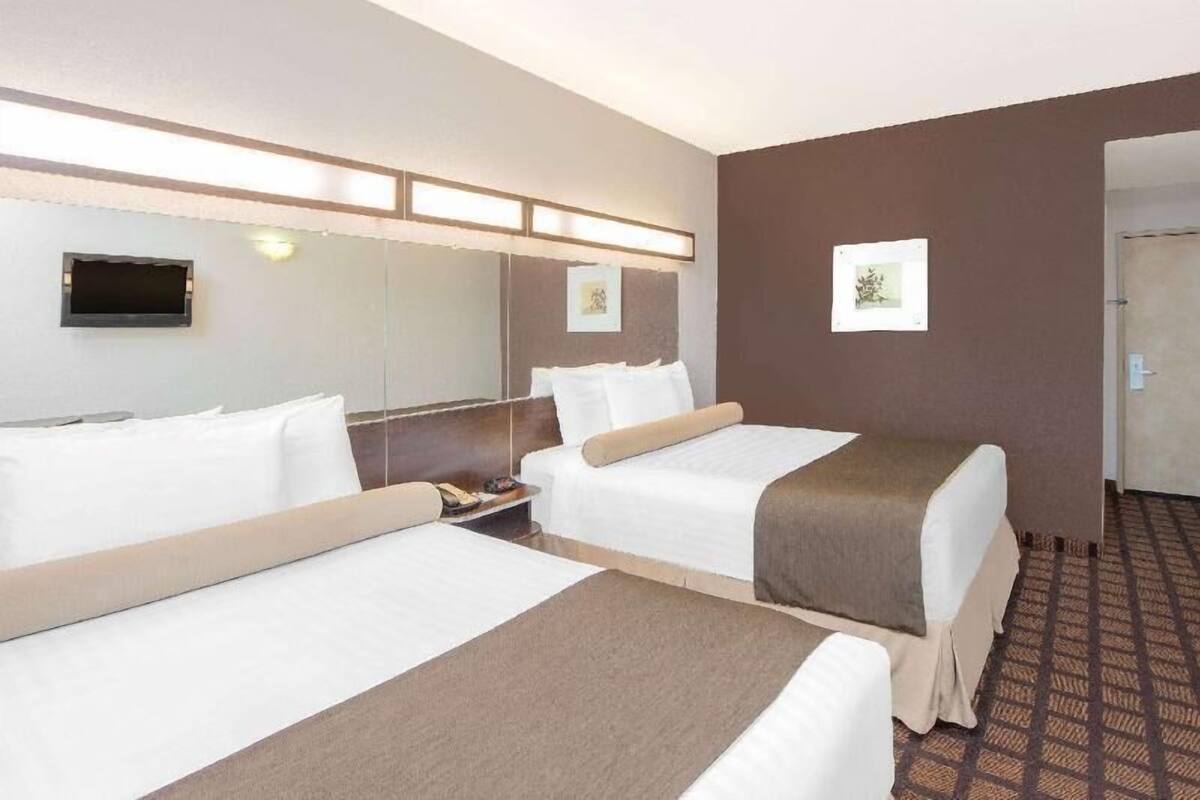 Ein Hotelzimmer mit zwei Betten, einem Flachbildfernseher, einem Nachttisch und einer Wandleuchte.