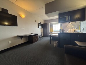 A compact hotel room with a kitchenette, a desk, a chair, a bed, and a window with curtains. - Microtel Inn & Suites by Wyndham Quincy Downtown/River Area (Quincy)
