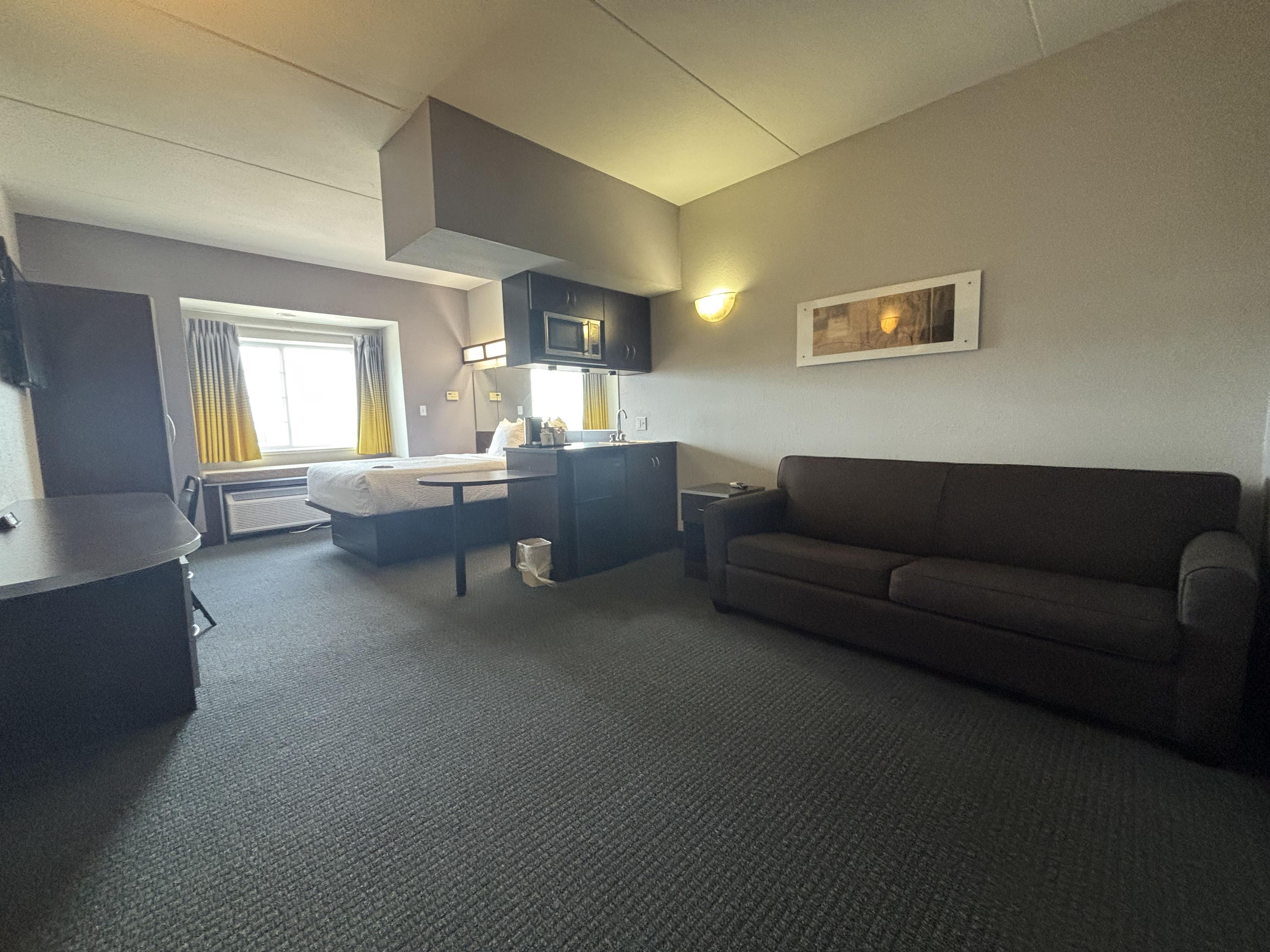 Habitación de hotel compacta con kitchenette, sofá, cama y una pequeña mesa.