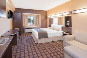 Una habitación de hotel con cama, escritorio, silla, televisor y ventana con cortinas.