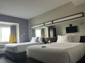 Une chambre d’hôtel avec deux lits, un grand miroir, un téléviseur à écran plat et une fenêtre avec des rideaux.