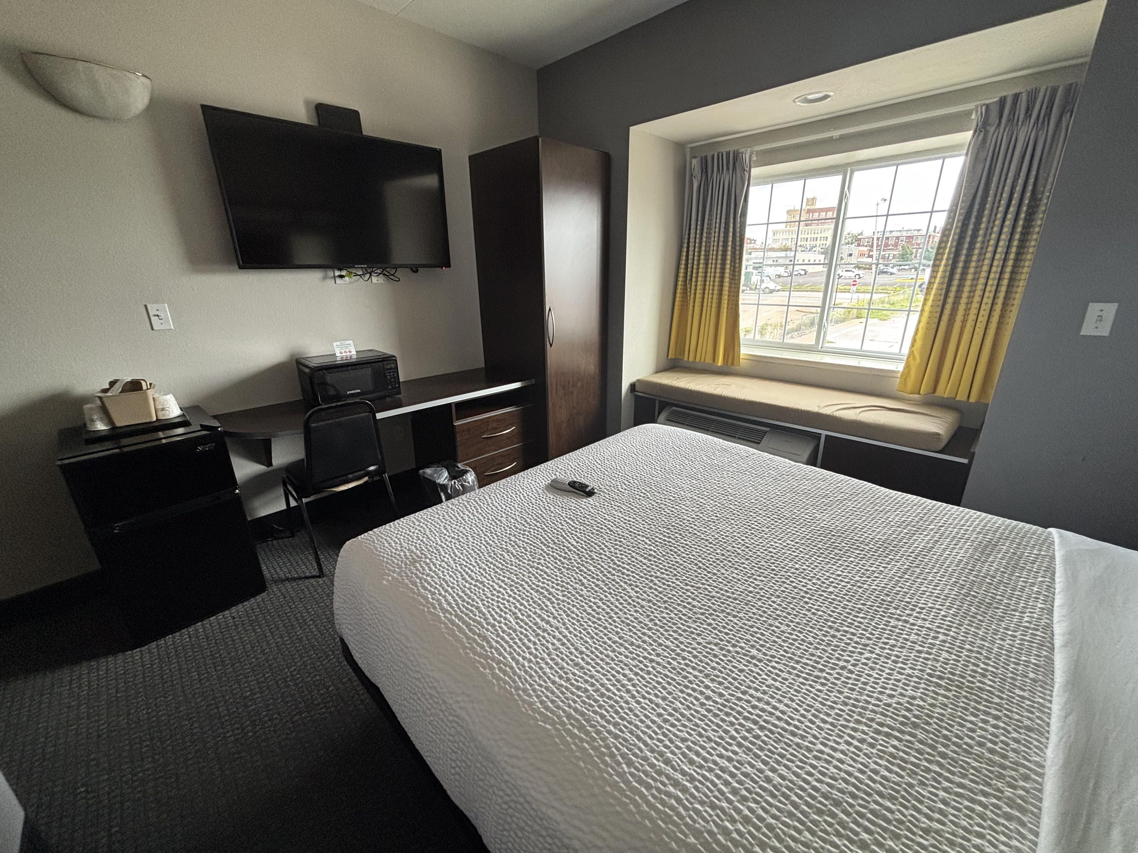 Une chambre d’hôtel équipée d’un lit, d’un bureau, d’une chaise, d’une télévision et d’une fenêtre avec des rideaux.
