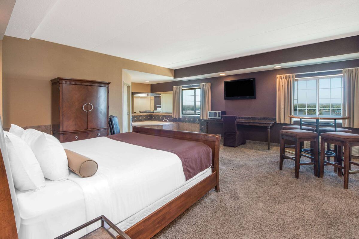 Ein Hotelzimmer mit einem großen Bett, einem Schreibtisch, einem Fernseher und Blick ins Freie.