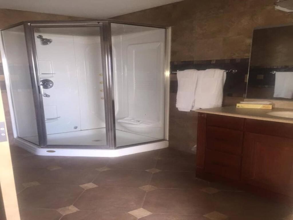 A corner shower enclosure, a wooden vanity with a mirror, and a tiled floor.