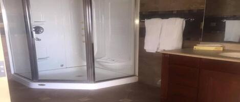 A corner shower enclosure, a wooden vanity with a mirror, and a tiled floor.