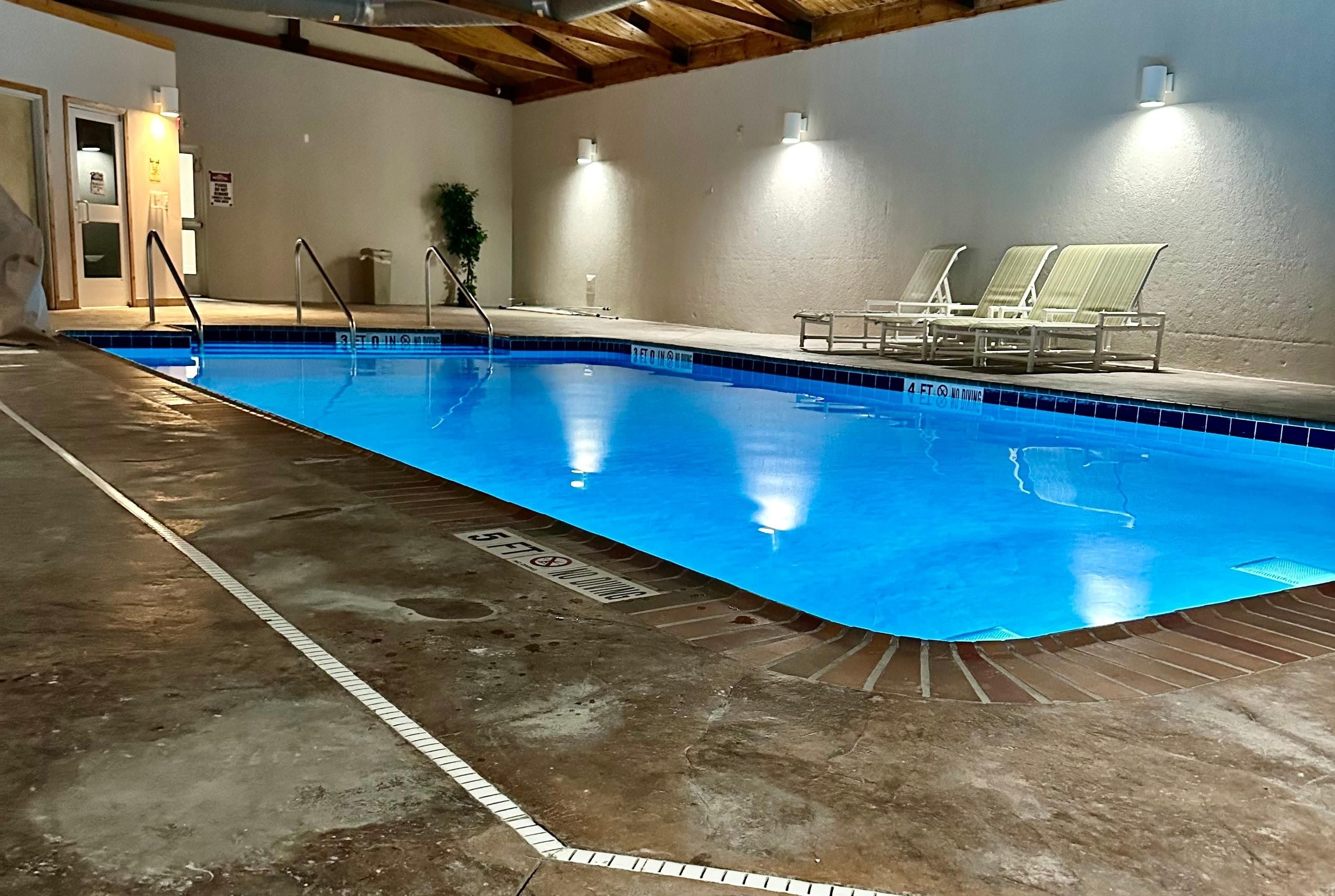 Piscina interior com indicador de profundidade de 0,9 metros, placa indicando que não é permitido mergulho em uma área de 1,2 metros e área ao redor da piscina com espreguiçadeiras.