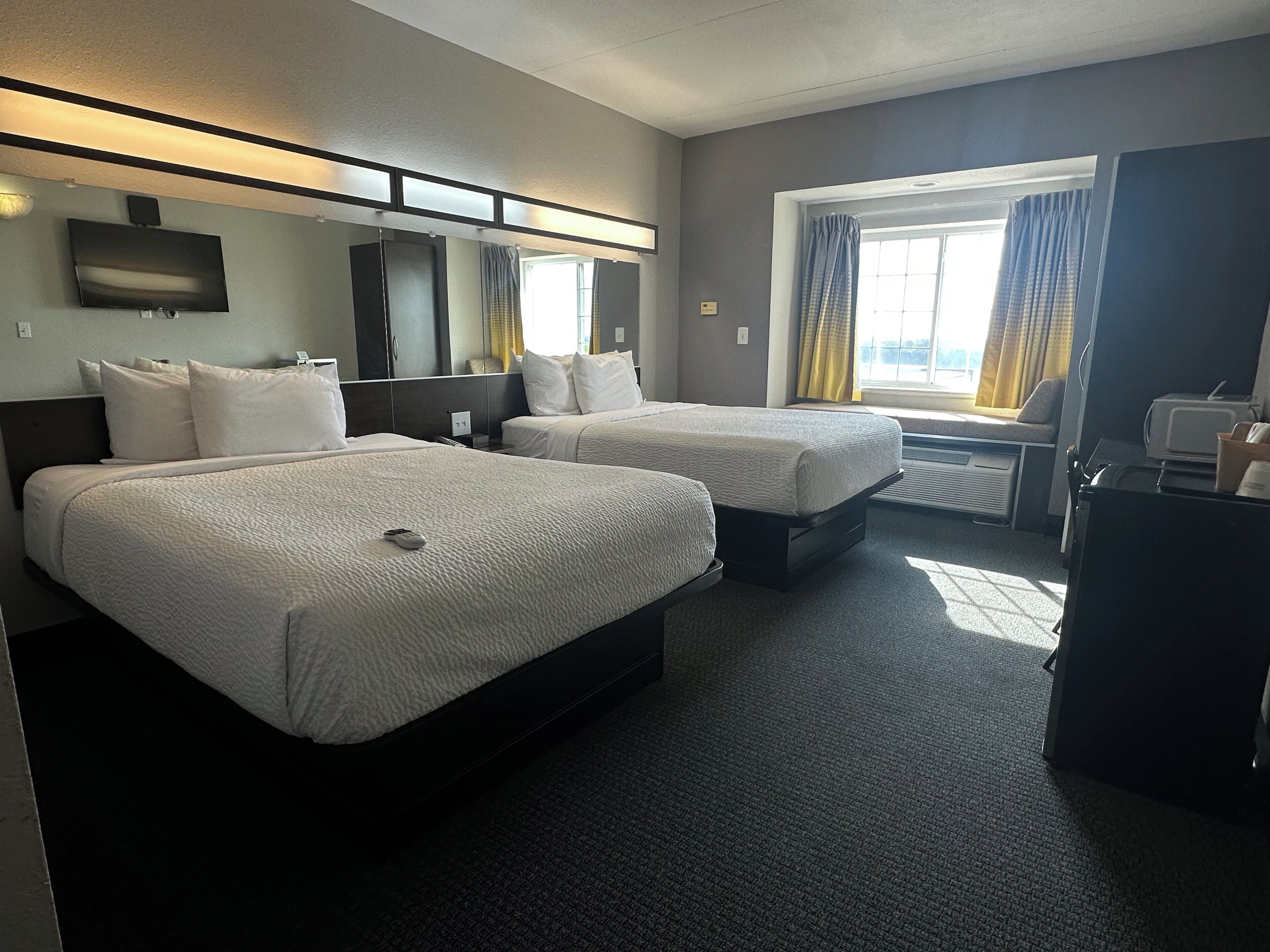 Ett hotellrum med två sängar, ett skrivbord, en TV och ett fönster med gardiner.