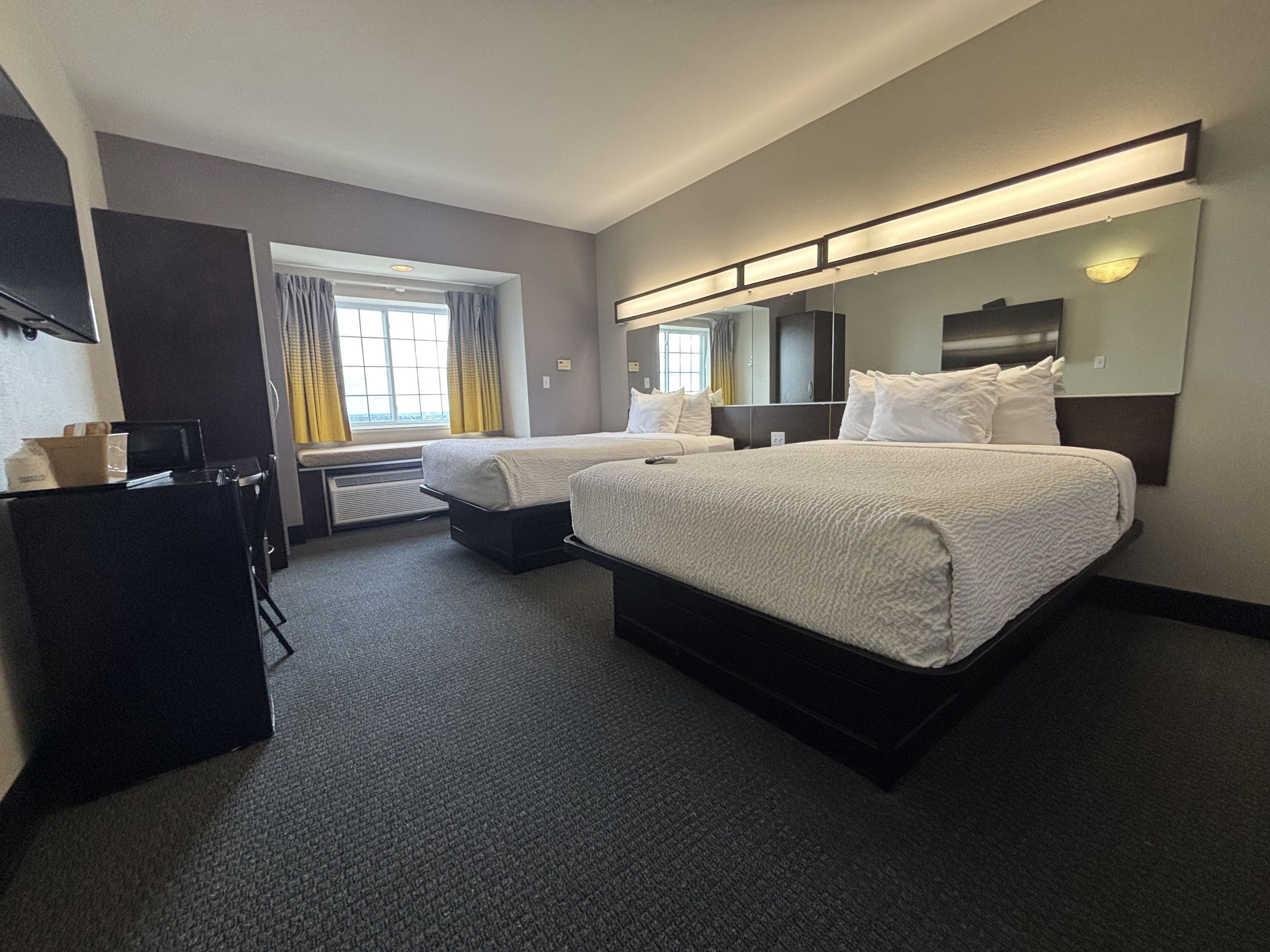 Habitación de hotel con dos camas, un escritorio y un espejo grande.