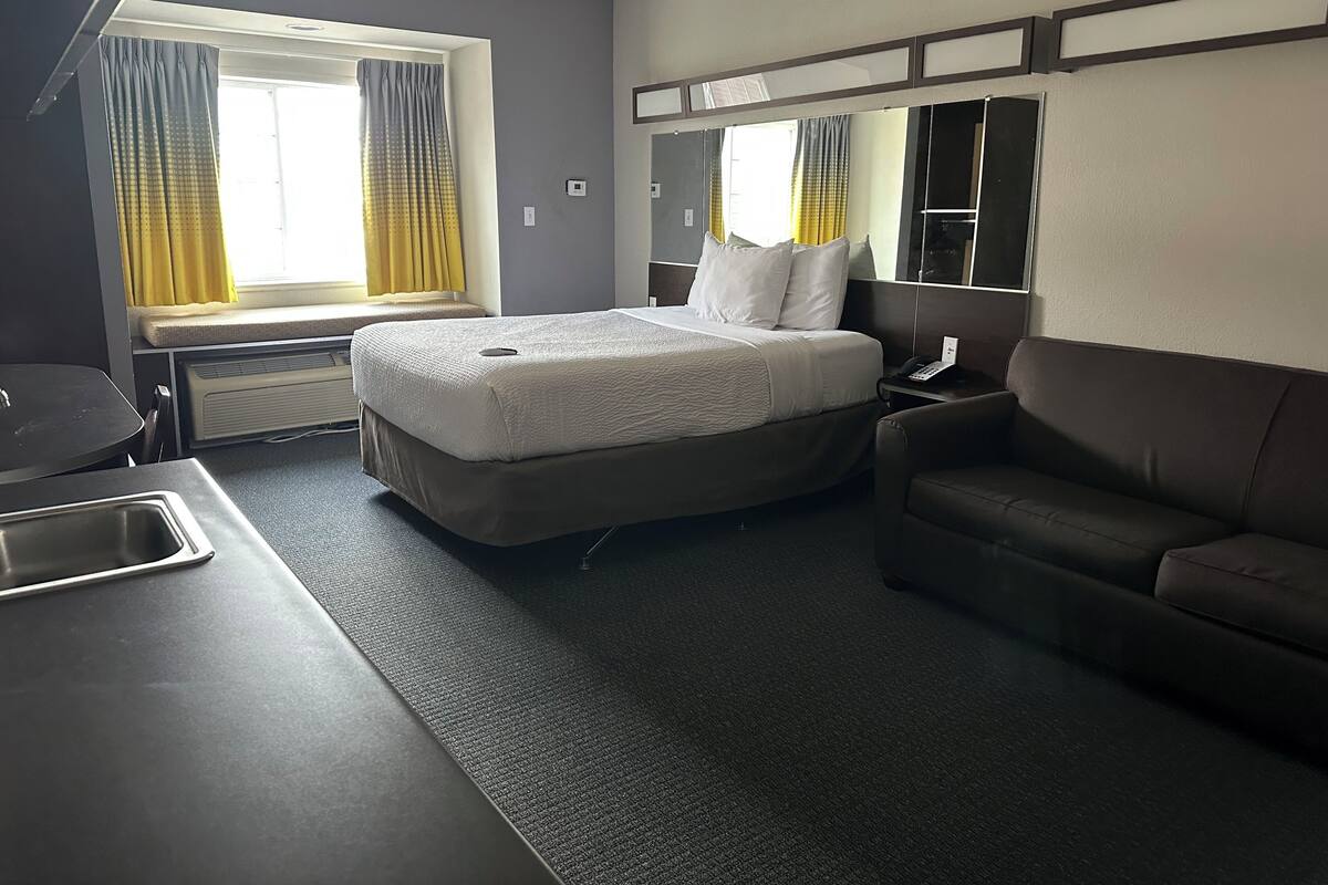 Ein Hotelzimmer mit einem Bett, einem Schreibtisch, einem Sessel, einem Spiegel und einem Fenster mit Vorhängen.