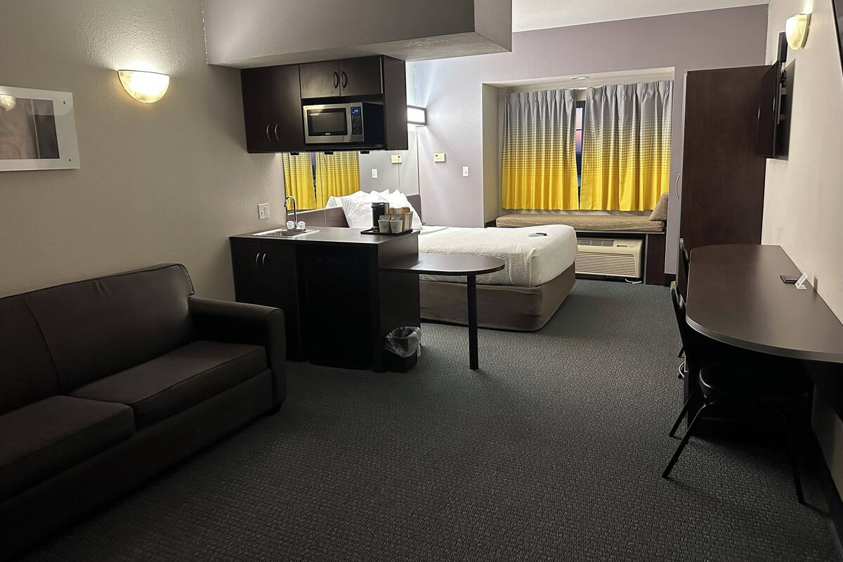 Ein kompaktes Hotelzimmer mit Küchenzeile, einer Couch, einem Bett und einem kleinen Tisch.
