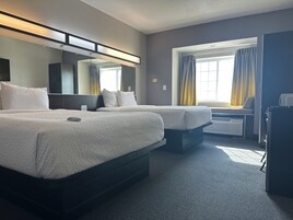 Habitación de hotel con dos camas, un escritorio, una silla, un espejo grande y una ventana con cortinas.